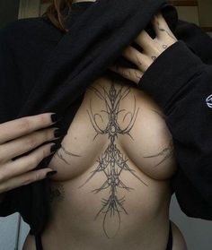 a woman with tattoos on her back holding onto a black hoodie and looking at the camera