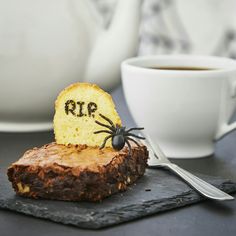 a piece of cake with a spider on it sitting next to a cup of coffee