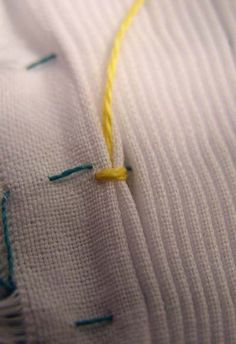 a close up view of a piece of white fabric with yellow thread on the end