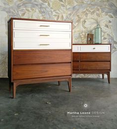 two wooden dressers sitting next to each other in front of a floral wallpaper