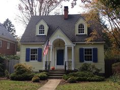 a small yellow house with blue shutters and an american flag on the front door