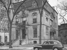 an old black and white photo of a car parked in front of a large building