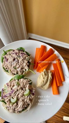 a white plate topped with two sandwiches covered in tuna and veggies next to carrots