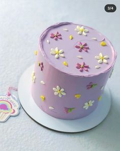 a purple cake with white and yellow flowers on it sitting on a plate next to a tag