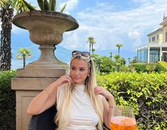 a woman sitting on a chair next to a glass of orange juice and a potted plant