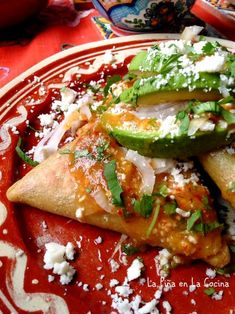 mexican food on a red plate with white and green garnishments, including avocado