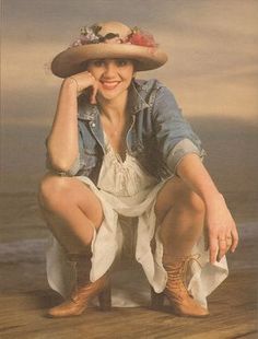 a woman wearing a cowboy hat sitting on top of a wooden floor next to the ocean