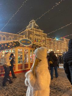 a woman in a white fur coat looking at christmas lights on the building behind her