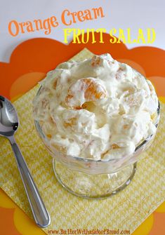 an orange cream fruit salad in a glass bowl with a spoon on the side,