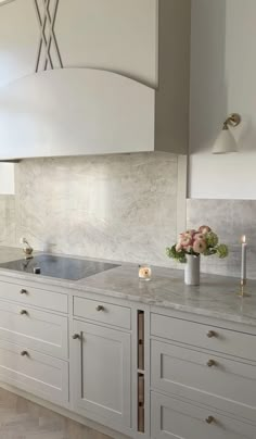 a kitchen with white cabinets and marble counter tops, candles and flowers in a vase