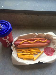 a hot dog and french fries on a tray with a drink next to it at a fast food restaurant