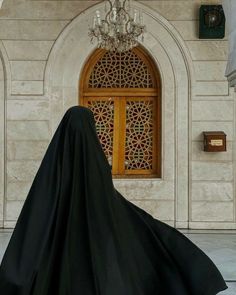 a woman wearing a black veil standing in front of a building with a chandelier