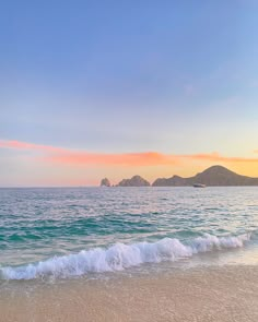 an ocean beach with waves coming in to shore and mountains in the distance at sunset