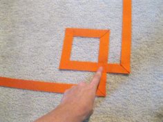 someone is making an origami frame out of orange strips on the floor with their finger