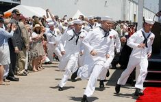 men in white uniforms are walking down the red carpet as people watch from behind them