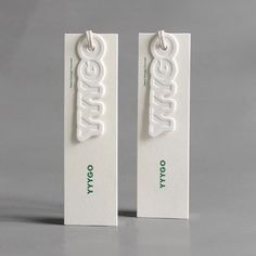 two white tags with green letters on them sitting next to each other in front of a gray background