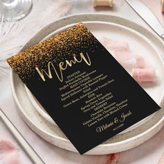 a black menu card with gold glitter on it sitting on a white plate next to silverware