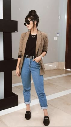 a woman standing in front of a black and white wall wearing jeans, a plaid blazer