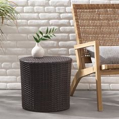 a wicker table with a vase on it next to a chair and potted plant