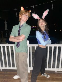 two young people wearing bunny ears standing next to each other on a deck at night