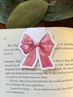 an open book with a pink bow on it