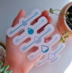 a hand holding some stickers near a potted plant on a white table with succulents