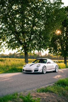 a white sports car parked on the side of a road next to trees and grass