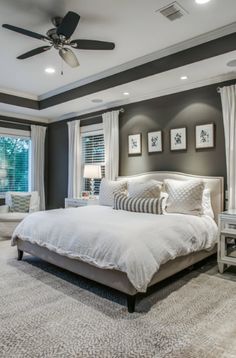 a bedroom with gray walls and white bedding, carpeted flooring and ceiling fan