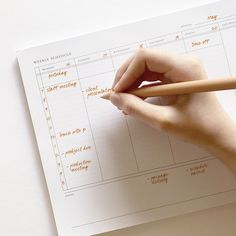 a person's hand writing on a planner with a pencil