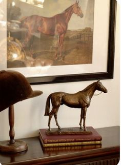 a brown horse statue sitting on top of a wooden table next to a framed painting