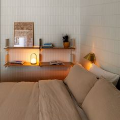 a bed sitting next to a wooden shelf with a lamp on it's side