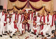 a group of men in white and red outfits posing for a photo together at a wedding