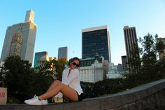 a woman sitting on the edge of a wall with her legs crossed and wearing sunglasses