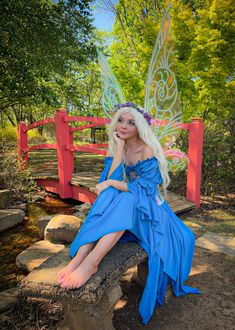 a woman dressed as a fairy sitting on a stone bench next to a red bridge