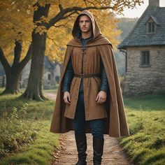 a man in a brown cloak and black boots is standing on a path near some trees