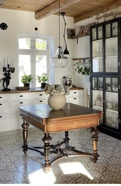 an old fashioned kitchen with white cabinets and wooden table in front of glass fronted cupboards