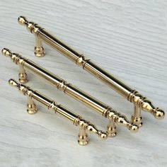 three brass - plated handles and knobs on a white wooden surface