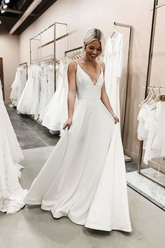 a woman standing in front of a rack of wedding dresses