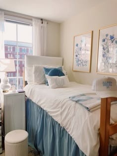 a white bed with blue and white sheets in a bedroom next to a large window