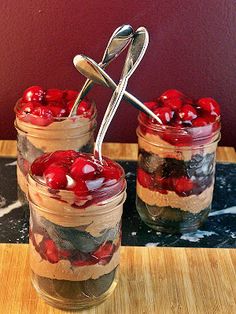 two jars filled with desserts sitting on top of a wooden table next to a spoon