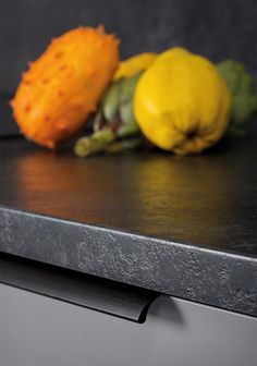 two lemons, one yellow and one green on a black counter top with other fruit