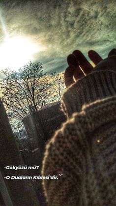 a person holding their hand up to the sky with trees in the background and clouds overhead