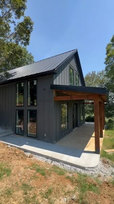 a small house with a covered patio in the middle of some grass and trees behind it