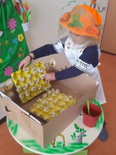 a young child is playing with an open cardboard box filled with honey cubes on a table