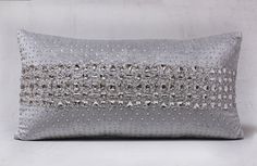 a silver pillow with sequins on the front and back, sitting against a white wall