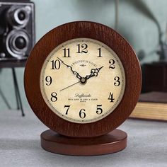 a wooden clock sitting on top of a table next to a book and speaker system