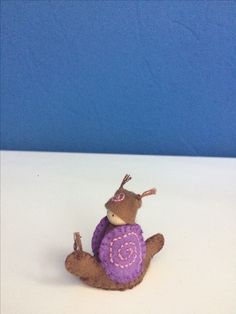 a small stuffed animal with a purple sweater on it's back, sitting on a white surface