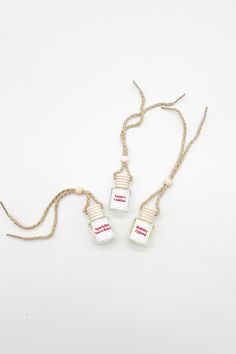 three small glass bottles are hanging from a gold chain on a white surface, one is empty and the other has red lettering