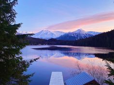 a lake with mountains in the background and a dock at the end that is surrounded by pine trees