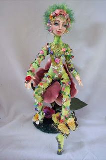 a doll with green hair and flowers on her head sitting on top of a flower pot